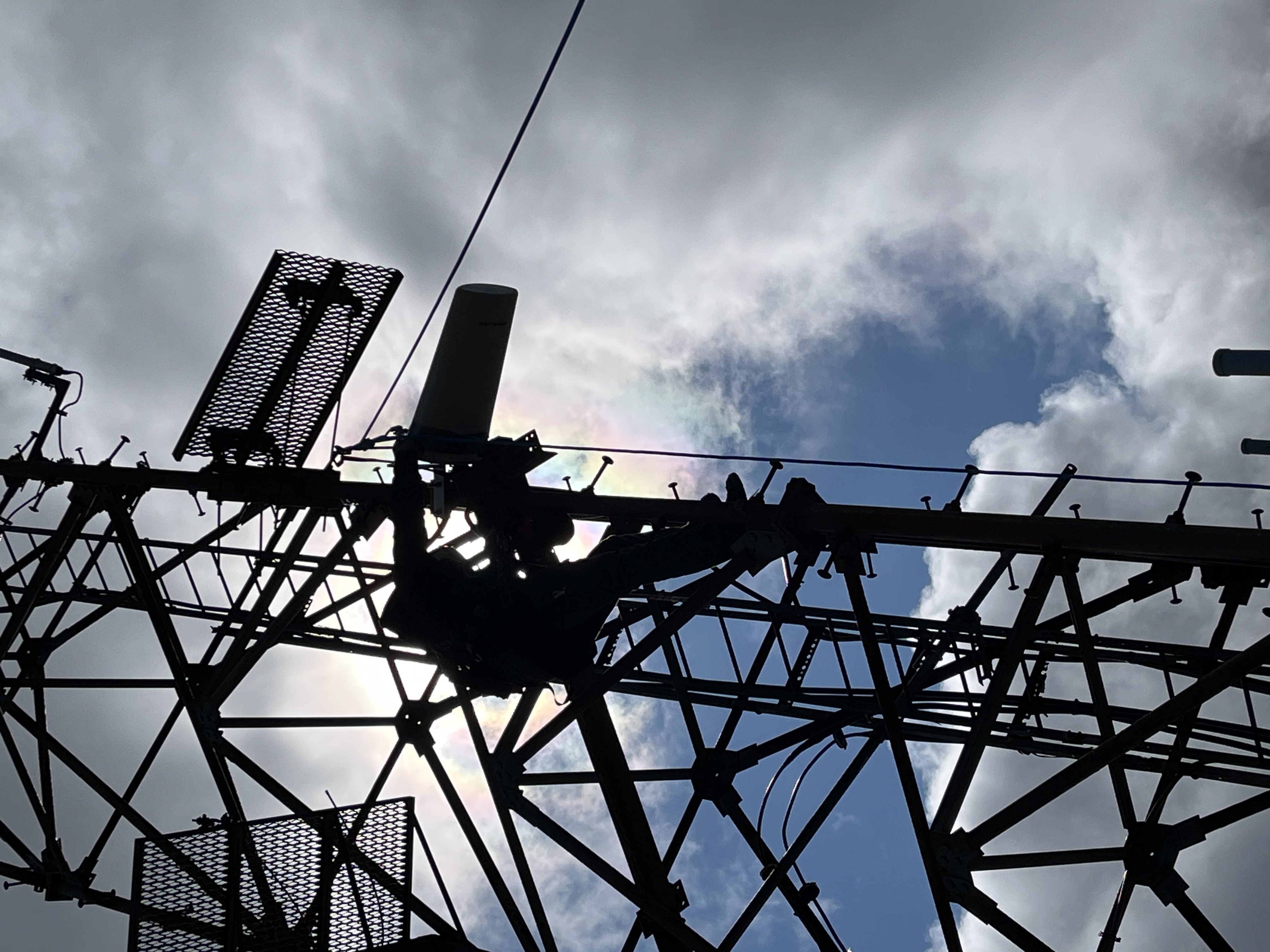 Silhouette of person on communications tower attaching antenna with cover.