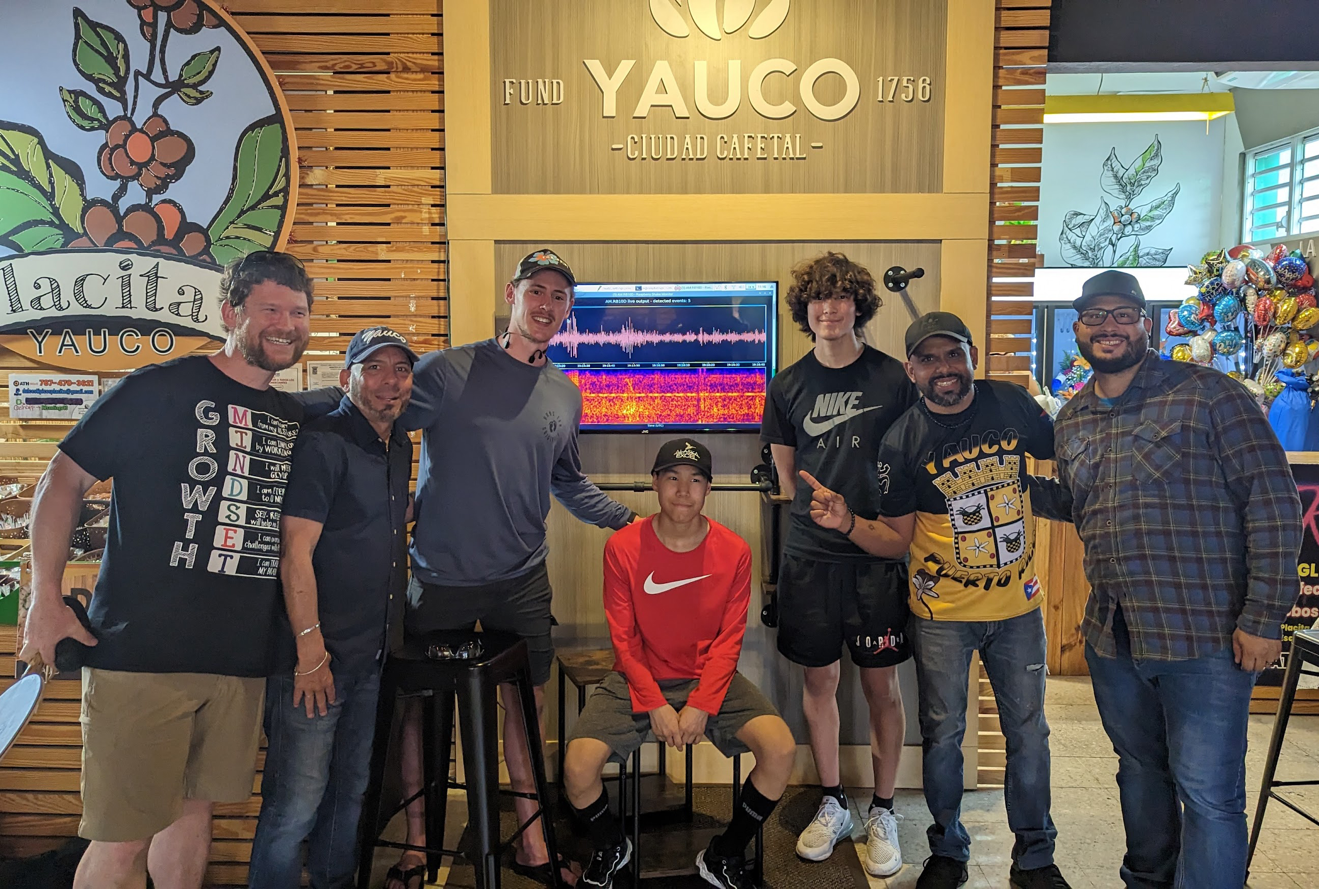 Students and instructors pose in front of screen displaying seismogram in coffee shop.