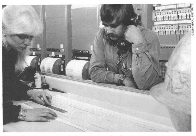 Black and white photo of woman measuring paper seismograph with ruler, man holding phone handset.