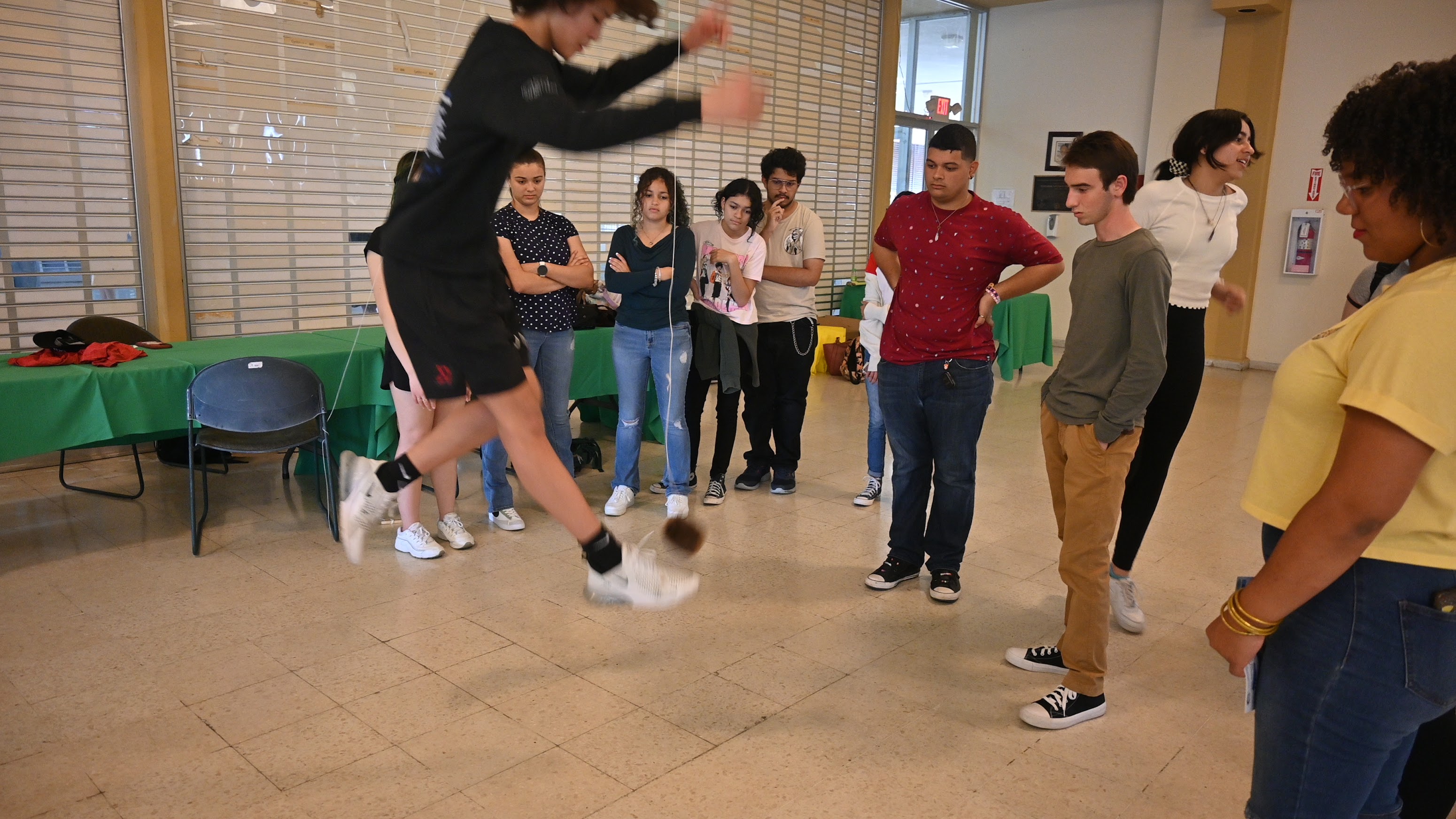 High school student jumping to kick ball suspended from ceiling while other students watch.