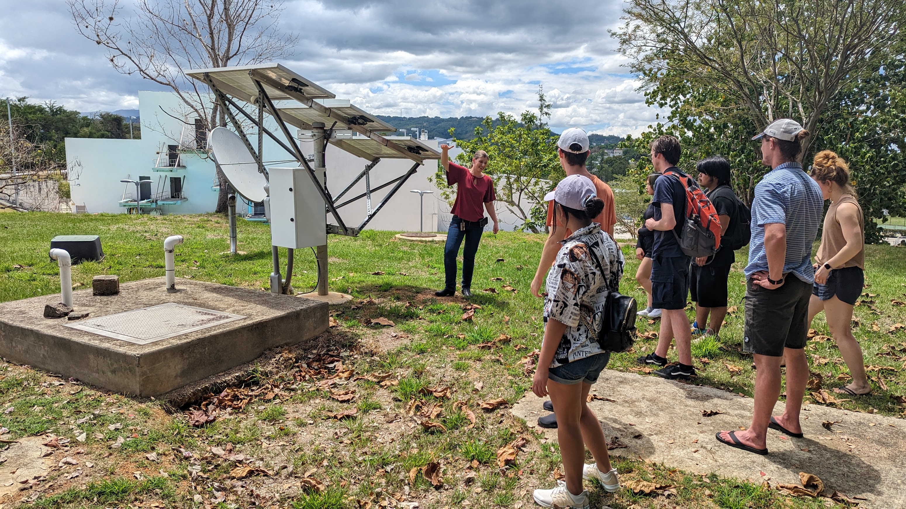 Woman gesturing to seismology station outside in front of student group. 